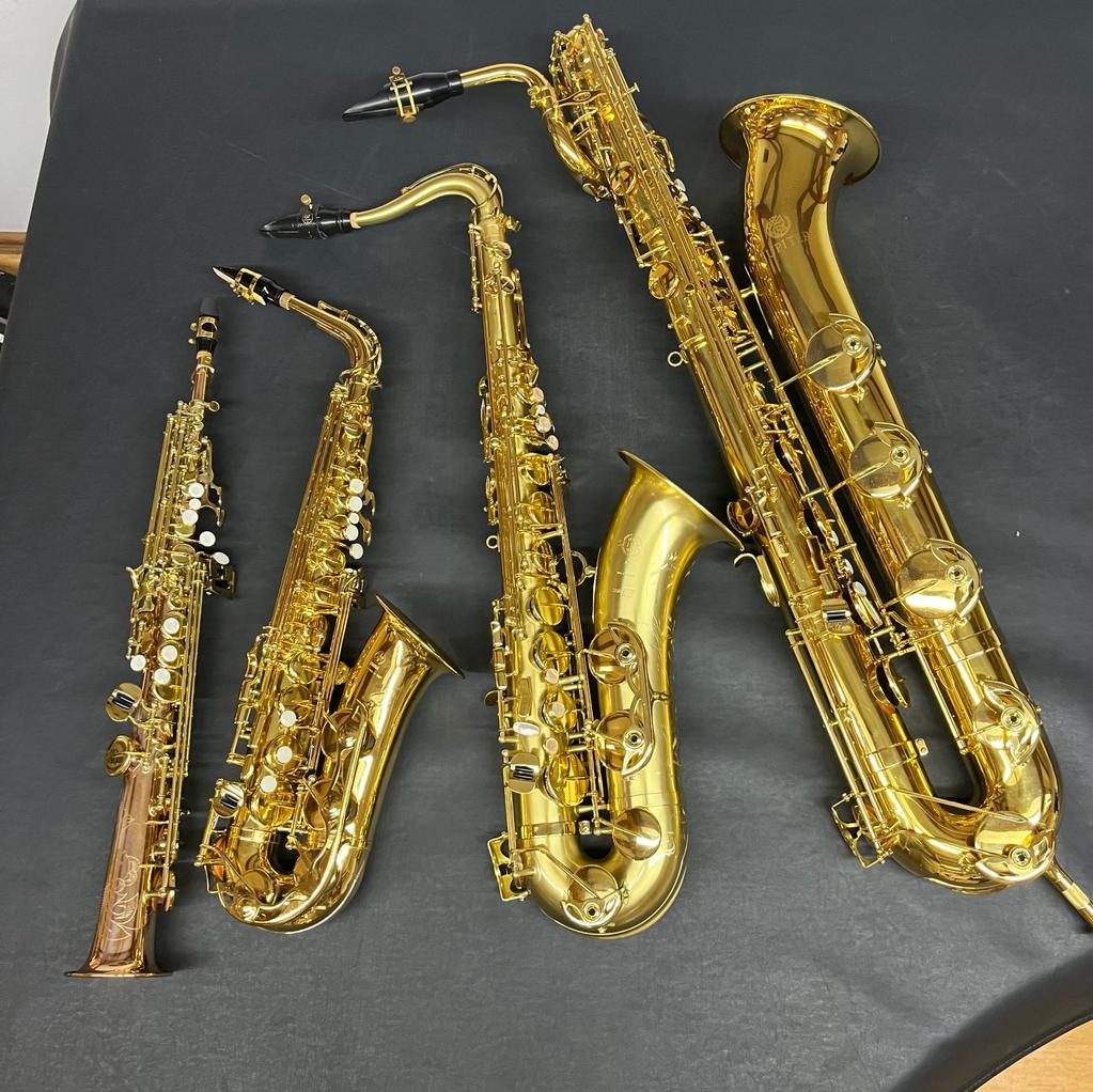 Auf schwarzem Untergrund liegen vier verschieden große Saxophone. 