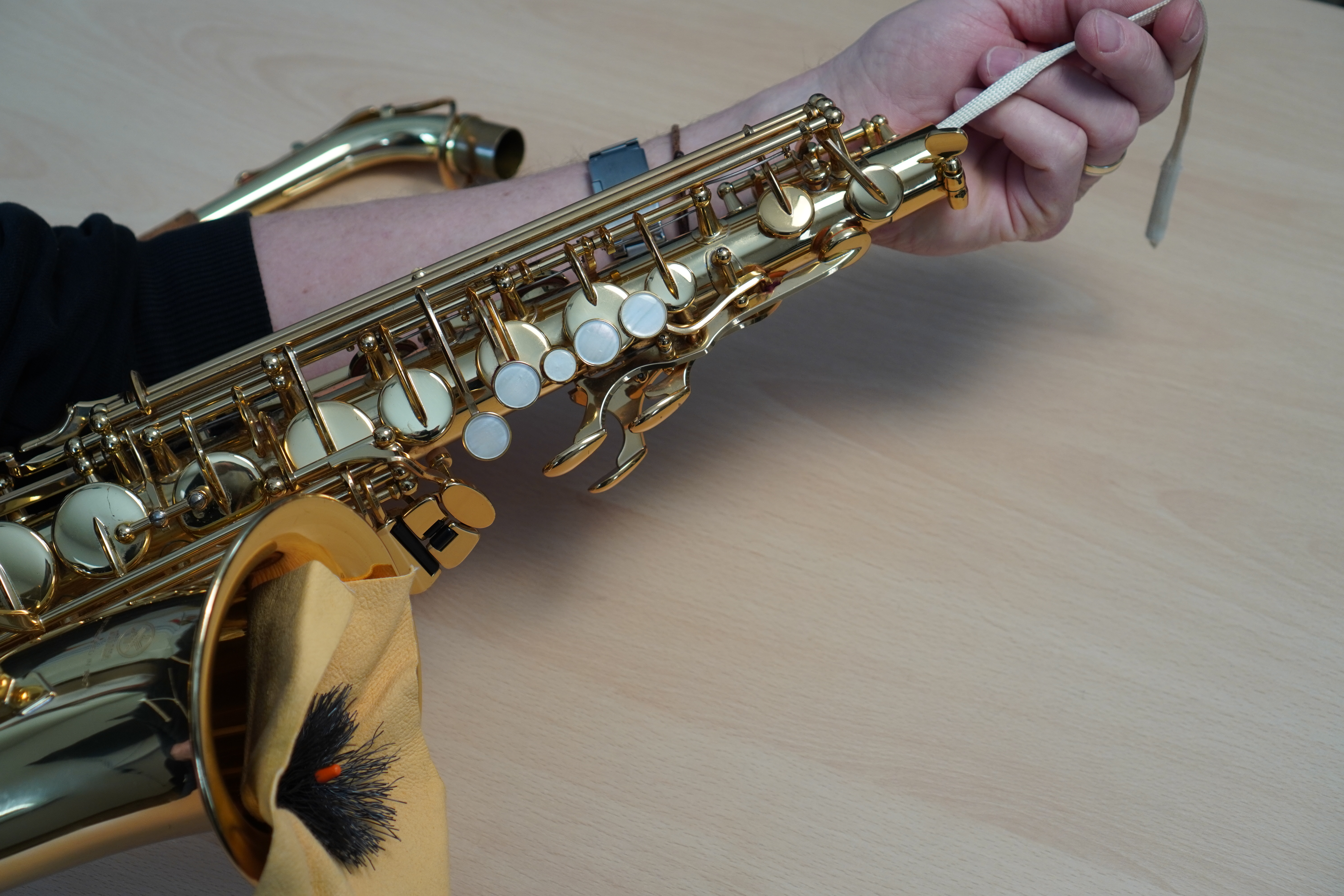 Ein Mensch putzt ein Saxophon mit einem Durchzieh-Wischer. 